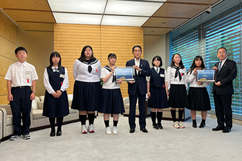 岸田内閣総理大臣が中央に立ち、その両脇に学生が数名並んでいる写真