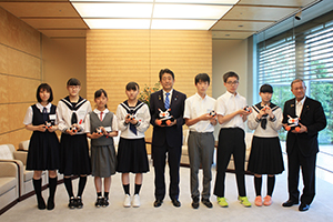 安倍内閣総理大臣が中央に立ち、その両脇に学生が数名並んでいる写真